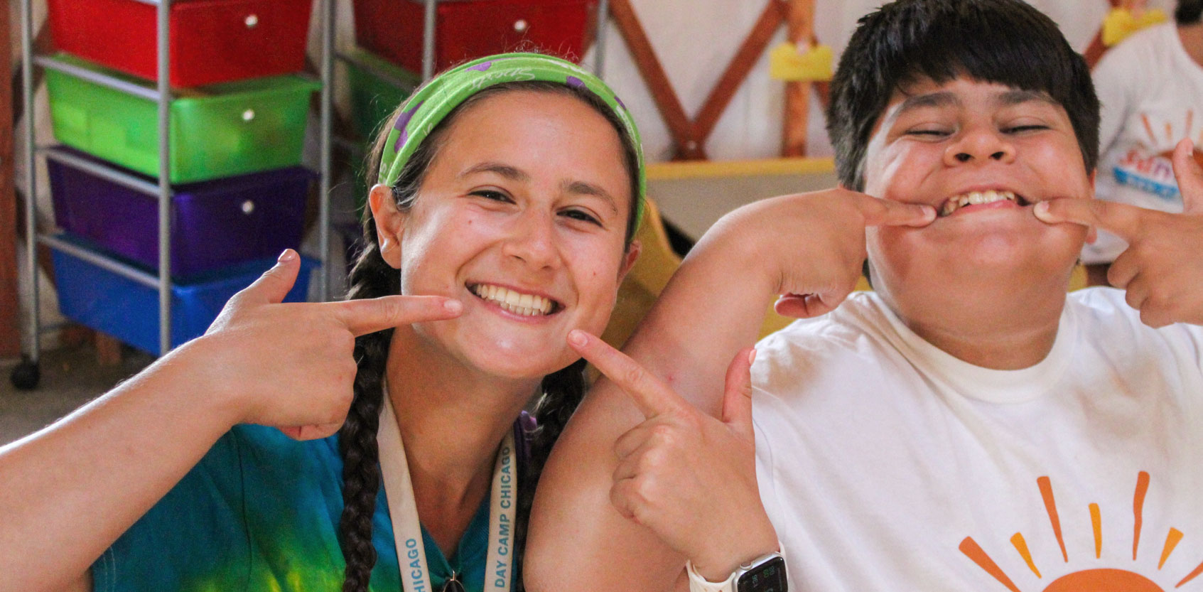 camper and counselor smiling with fingers at the corners of their mouths